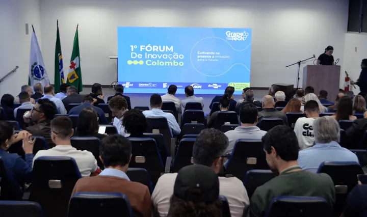 Plateia lotada no auditório do 1º Fórum de Inovação de Colombo, com o telão de abertura ao fundo