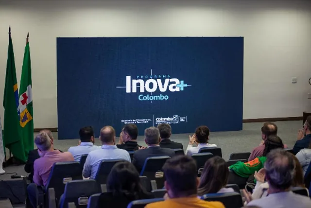 Plateia sentada em auditório diante de um telão com a marca Inova+ Colombo